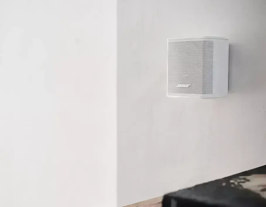 Динаміки Bose Surround Speakers встановлені на полицях у сучасному інтер'єрі вітальні